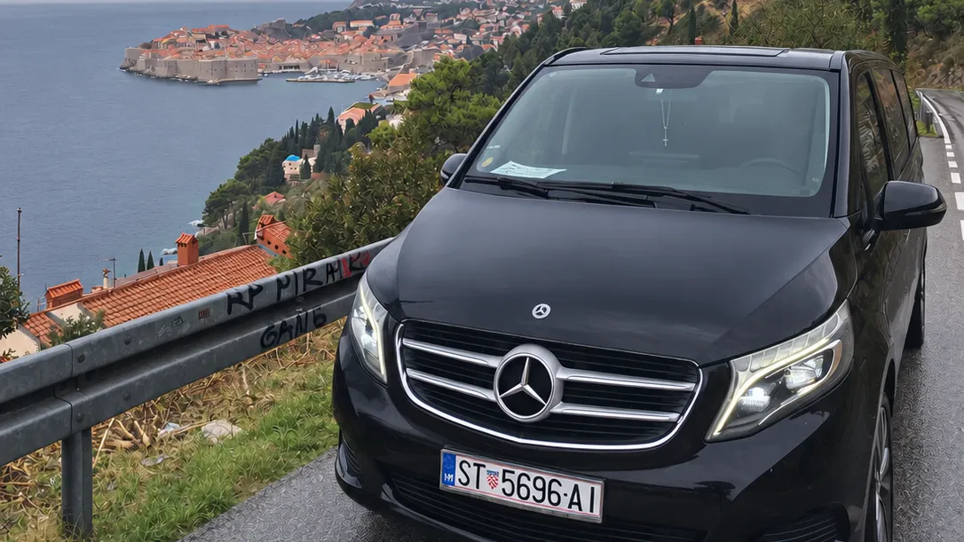 Black Mercedes-Benz V-Class on the coastal road above Dubrovnik, with the old town behind